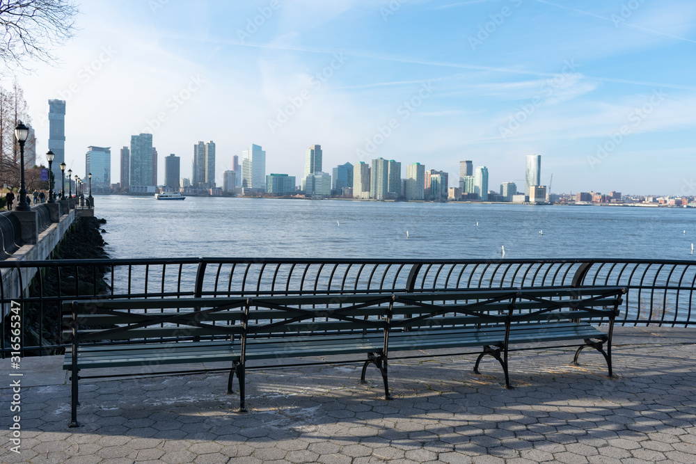 Empty Bench at Battery Park in New York City with a view of the Jersey City Skyline along the Hudson River