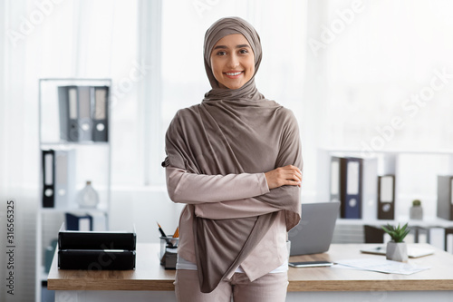 Fotografie, Obraz Confident Muslim Businesswoman Standing With Folded Arms Near Workplace In Offic