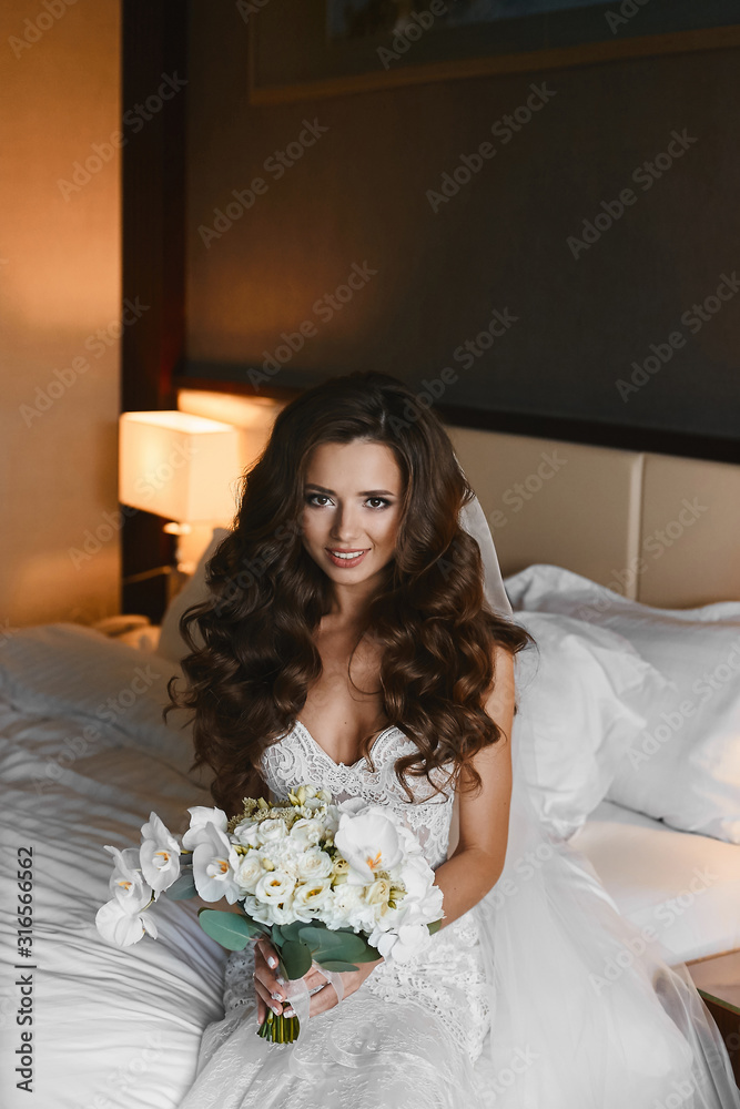 Young brunette woman with wedding hairstyle in a lace dress keeps a bouquet of phalaenopsis, roses and peonies flowers in hands. Stunning model girl in wedding dress holding bouquet of exotic flowers