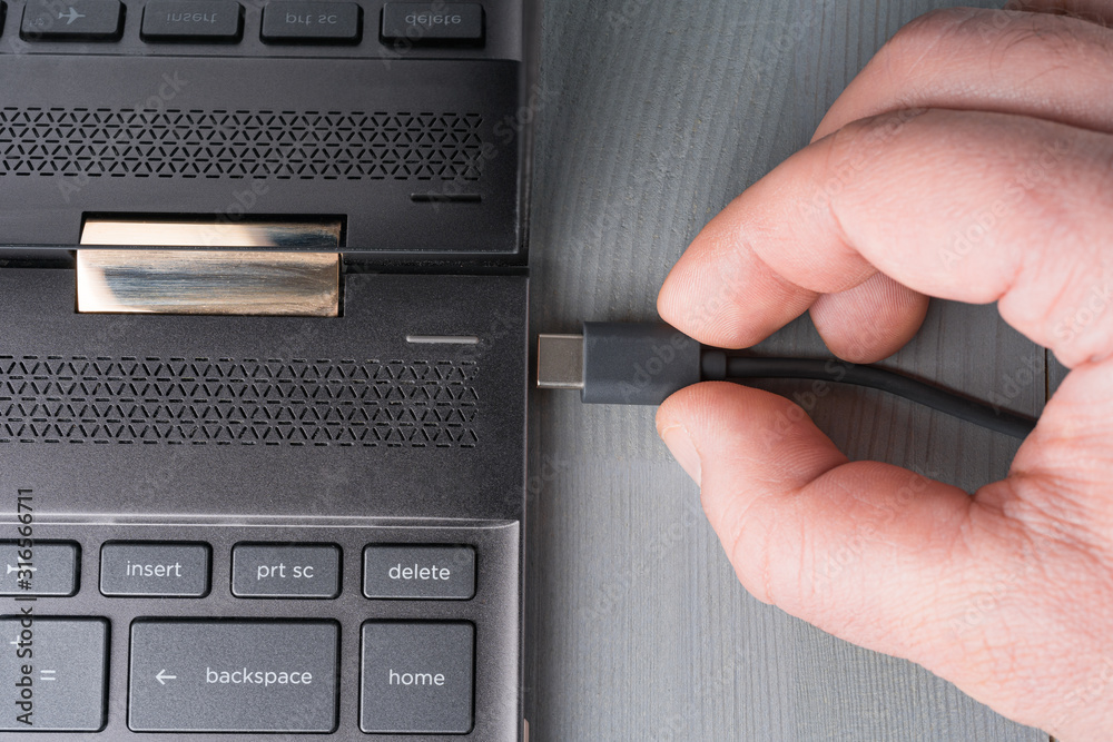 USB Type C grey cable being connected to the laptop computer. Flat lay top view.