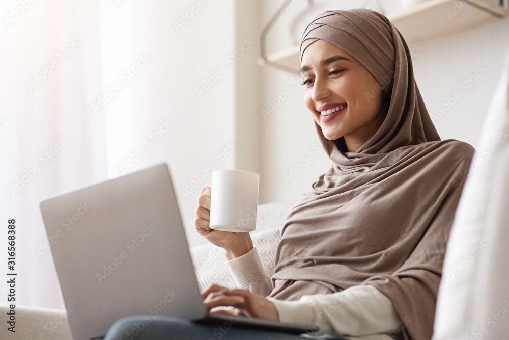 Muslim Woman In Hijab Using Laptop And Drinking Coffee At Home Stock ...