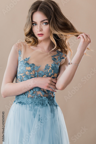 Pretty female model portrait in elegant blue lace dress on beige background