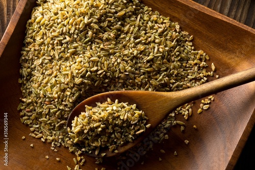 Uncooked, raw freekeh or firik, roasted wheat grain, on wooden plate with wood spoon on brown table background photo