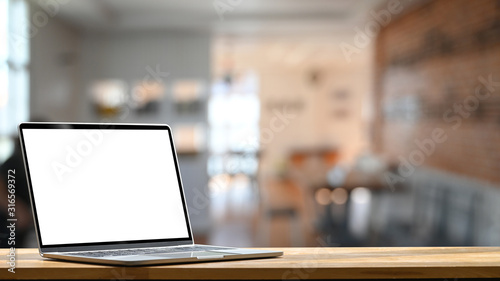Photo of modern laptop with white blank screen display setting on the wooden table over the blurred modern room.