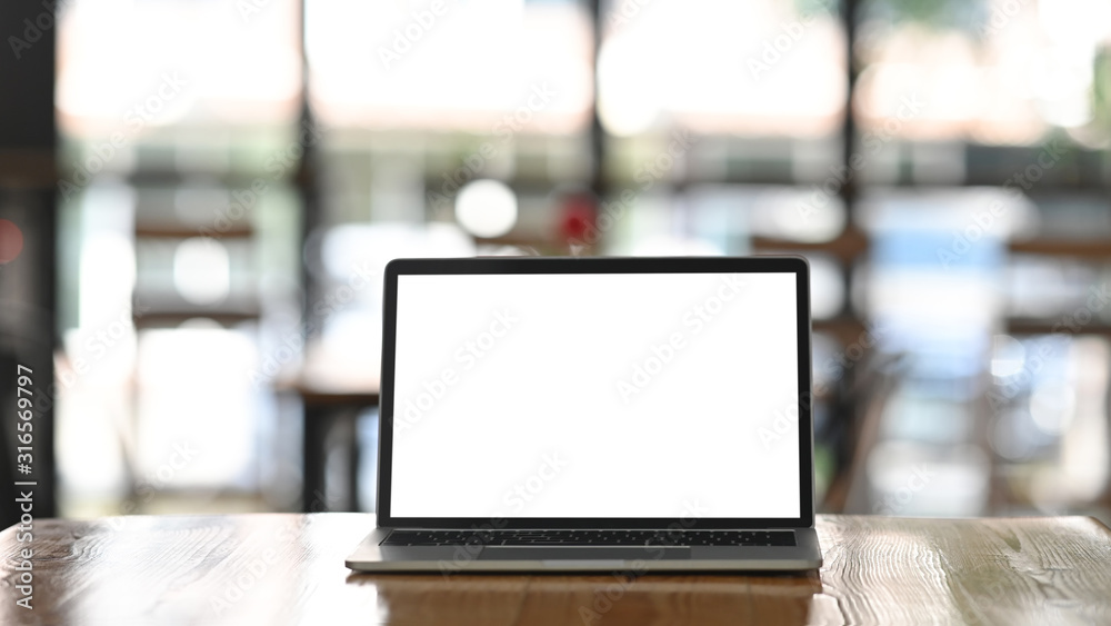 Front shot of modern laptop with white blank screen display setting on the wooden table over the blurred modern cafe. - obrazy, fototapety, plakaty 