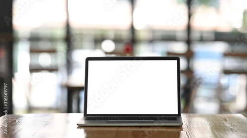 Front shot of modern laptop with white blank screen display setting on the wooden table over the blurred modern cafe.