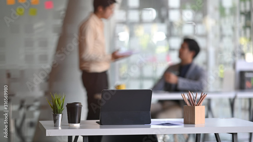 Front shot of working desk over the young business development team talking/discussing/brainstorming about them business at the modern office as background.