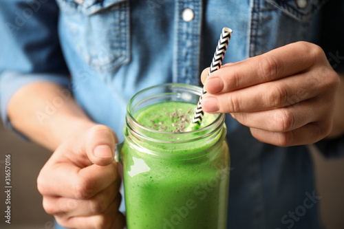 Woman holding tasty kale smoothie on brown background, closeup