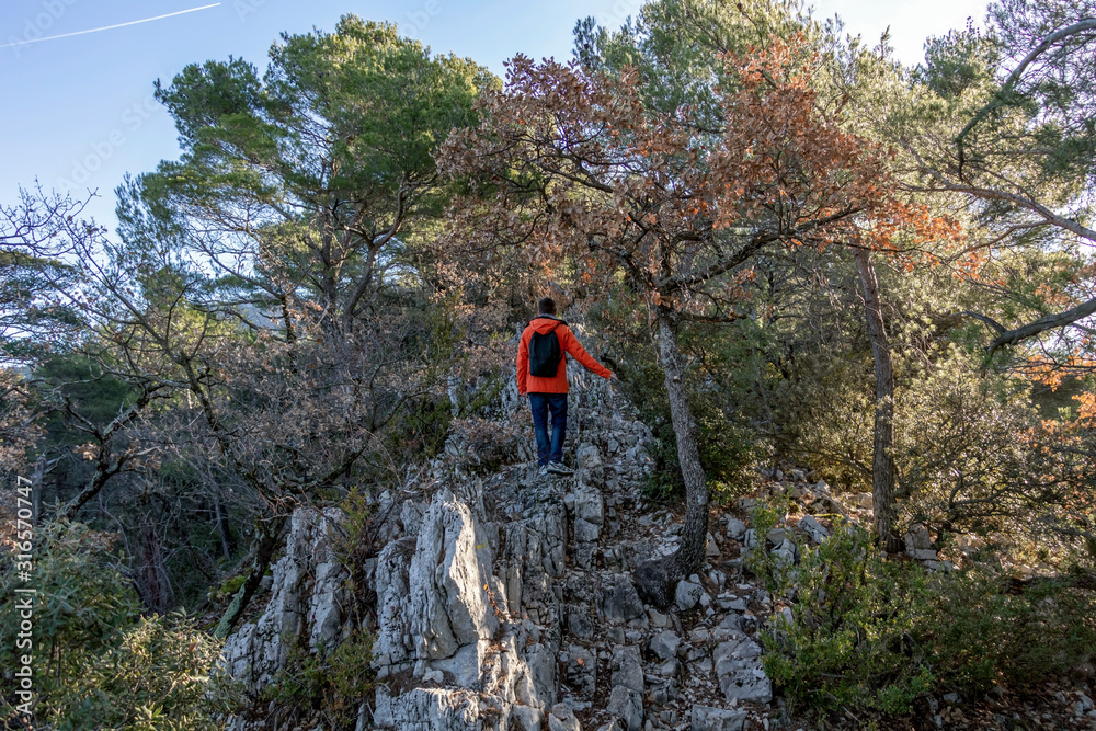 Young casual man climbing gray rock cliffs in sunny winter day in Provence, France, Europe