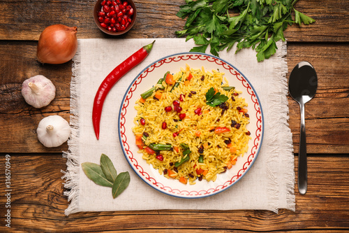 Tasty rice pilaf with vegetables served on wooden table, flat lay