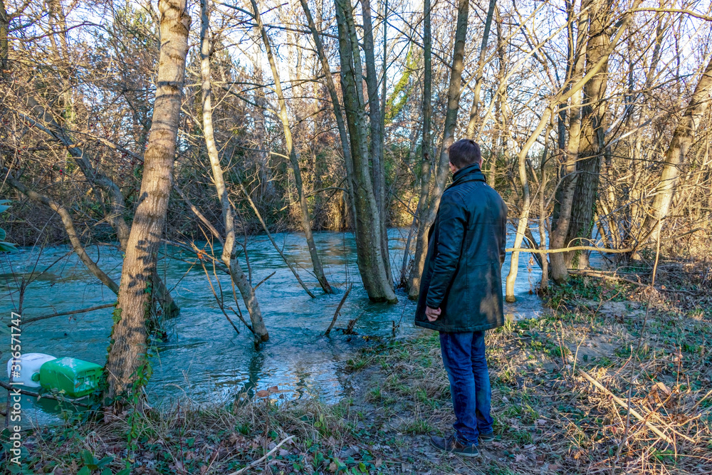 Young man looking aside of river with plastic bottles inside, polluted river in France