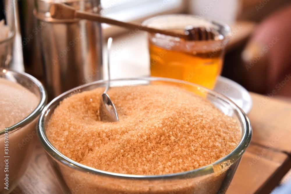 Additives to hot drinks. Cane sugar, white sugar and honey with a special wooden spoon with selective focus on blurred background. Unhealthy carbohydrates. Brown and white sugar, organic honey Additives to hot drinks. Cane sugar, white sugar and honey with a special wooden spoon with selective focus on blurred background. Unhealthy carbohydrates. Brown and white sugar, organic honey