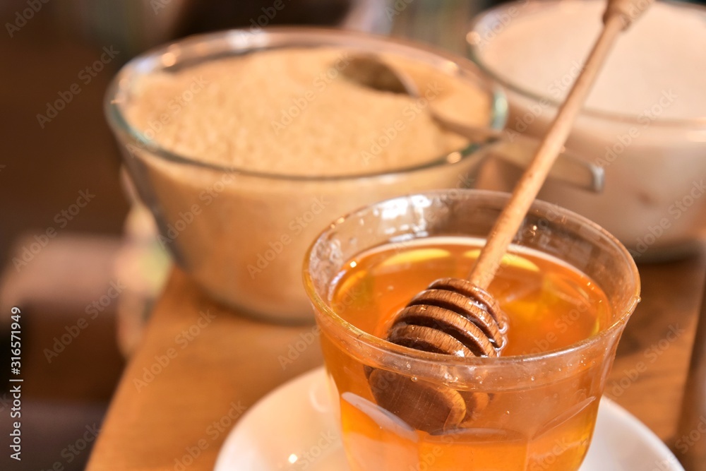 Additives to hot drinks. Cane sugar, white sugar and honey with a special wooden spoon with selective focus on blurred background. Unhealthy carbohydrates. Brown and white sugar, organic honey Additives to hot drinks. Cane sugar, white sugar and honey with a special wooden spoon with selective focus on blurred background. Unhealthy carbohydrates. Brown and white sugar, organic honey