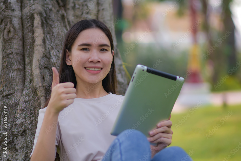 Fototapeta premium Asian Women holding tablet on social network and shopping online by internet sitting in city park