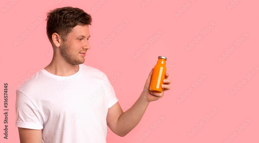 Attractive young man looking at bottle with orange detox drink Attractive young man looking at bottle with orange detox drink