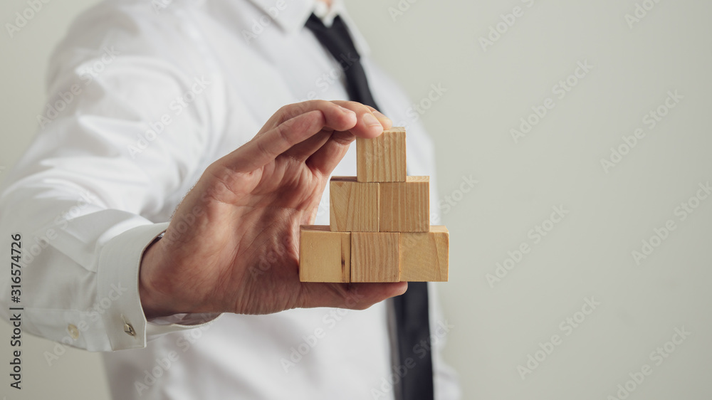 Businessman holding blank wooden blocks stacked in pyramid shape Businessman holding blank wooden blocks stacked in pyramid shape