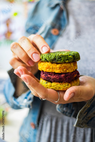 Vegan chickpea burgers cutlets or patties. Healthy vegan diet food. Woman holds in hand mixed vegetables yellow pumpkin, orange carrot, green spinach and red beet chickpea cutlets.