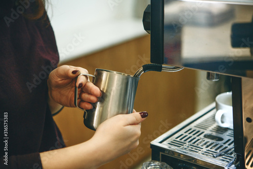 The process of making cappuccino in a coffee machine. Barista pours milk to add to coffee