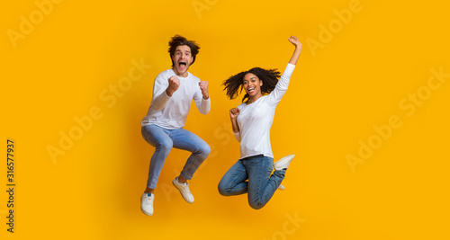 Overjoyed multiracial couple jumping in the air and celebrating success photo