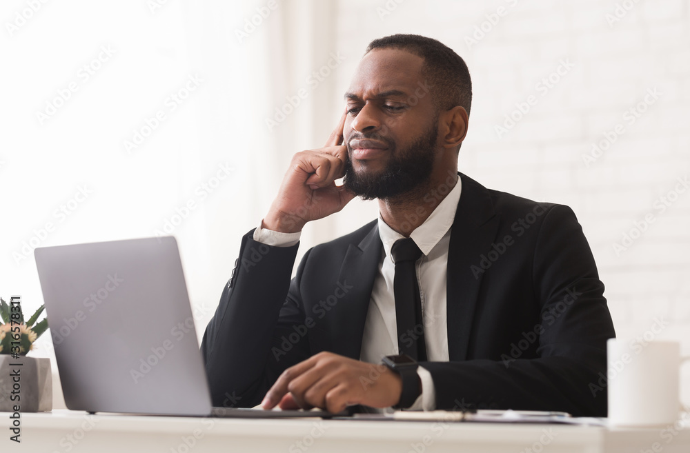 Pensive black businessman working with laptop in office Pensive black businessman working with laptop in office