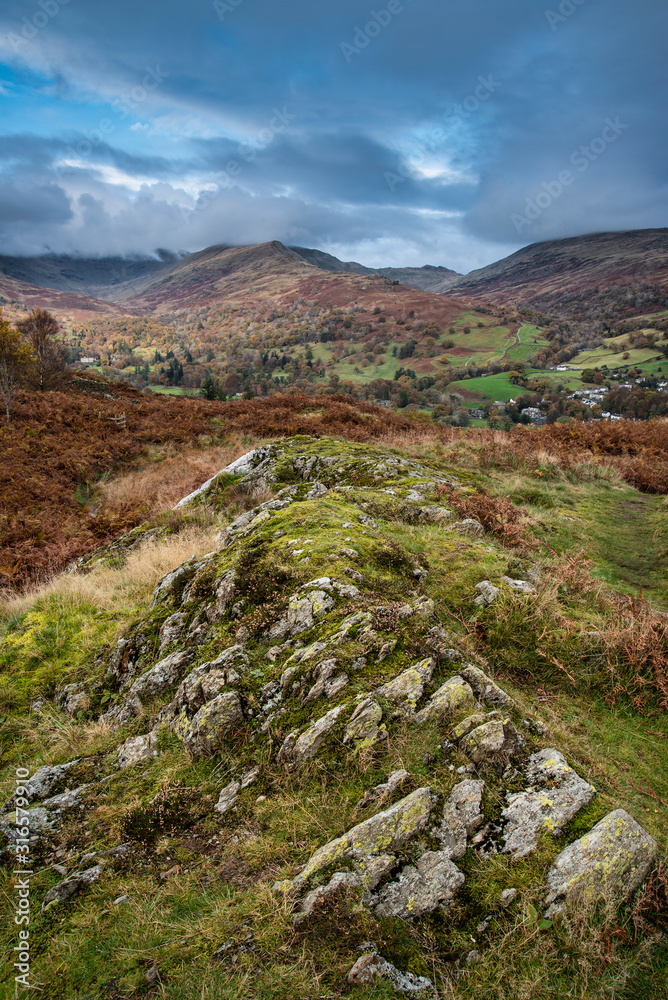 Beautiful colorful Autumn Fall landscape image of view from Loughrigg Brow towards mountains in distance with dramatic sky