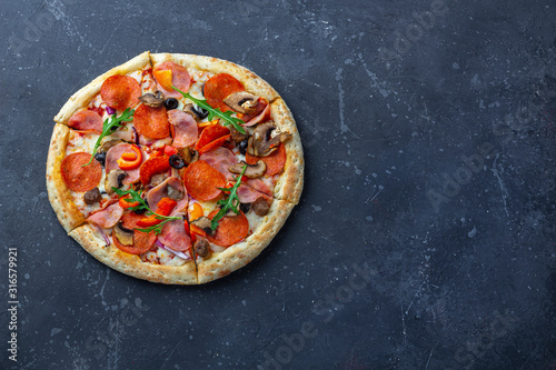 A fresh prepared pizza with salami, mushrooms, ham and cheese on a dark background. Italian traditional lunch or dinner. Fast food and street food concept. Flat ly, top view