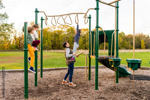 Mother assisting her daughter on the playgorund monkey bars