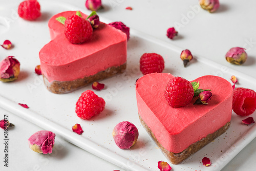 raw vegan heart shaped cakes or cheesecakes with fresh raspberries, mint and dried flowers. Valentines day dessert photo