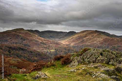 Beautiful colorful Autumn Fall landscape image of view from Loughrigg Brow towards mountains in distance with dramatic sky