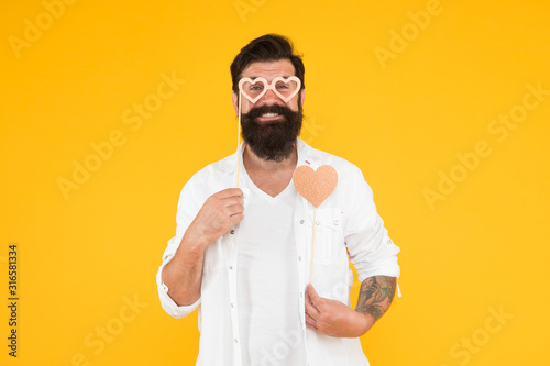 Just happy. brutal man with beard fall in love. romantic date. smiling male hipster in party glasses. bearded man hipster yellow background. love heart for valentines day holiday. happy birthday