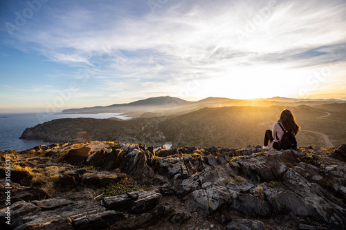 Beautiful woman standing on a cliff during sunset at Cap de Creus, Spain