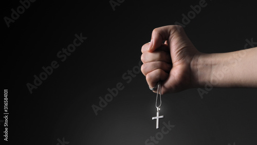 Close-up images of crucifix pendant and necklace in hand on black color background in studio which represent praying for god or jesus and thank gods for giving peaceful and faithful to people