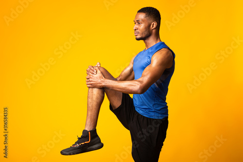 Young black sportsman walks highly holding knee