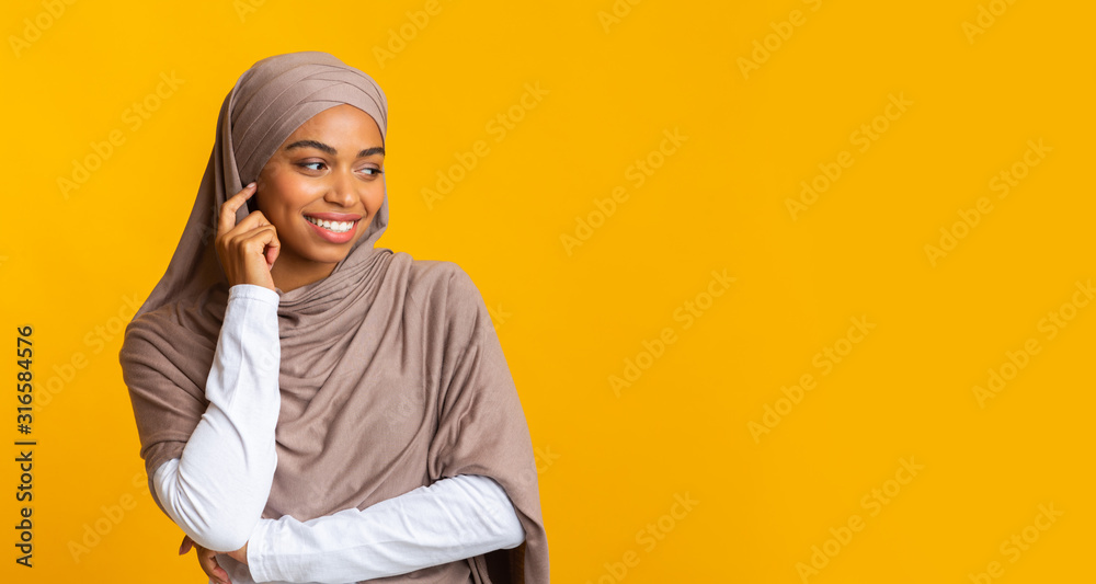 Interested black muslim girl looking away at copy space on yellow background Interested black muslim girl looking away at copy space on yellow background