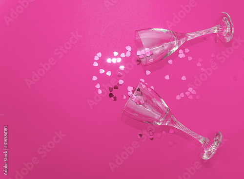 Flat lay celebration. Holiday concept for Valentine's Day, Christmas, New Year, birthday. Glasses for wine or champagne lie on a pink background and decorated with pink confetti hearts.