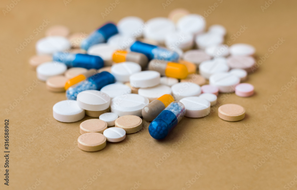 Heap of colorful pills, pharmaceutical medicine tablets and capsules on beige yellow background. Drug prescription for treatment medication health care concept, top view with copy space. Heap of colorful pills, pharmaceutical medicine tablets and capsules on beige yellow background. Drug prescription for treatment medication health care concept, top view with copy space.