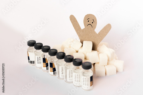 figure of a cardboard man surrounded by refined sugar cubes and bottles of insulin on white background, diabetes protection medical concept.