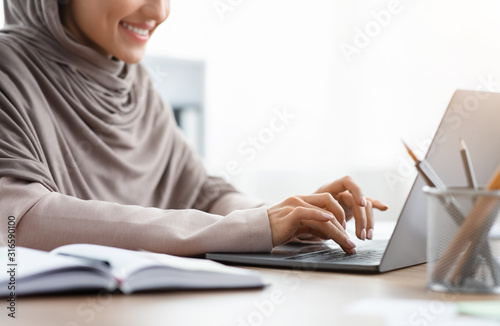Unrecognizable muslim woman in headscarf working on laptop in office