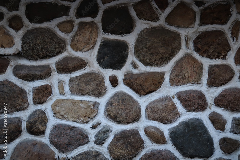 Fototapeta premium The surface is made of flat stones of black and brown shades, bonded with white plaster.