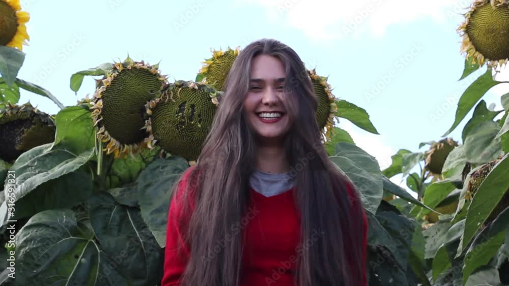Mujer joven sonríe mirando a la cámara con girasoles cielo a su espalda. 