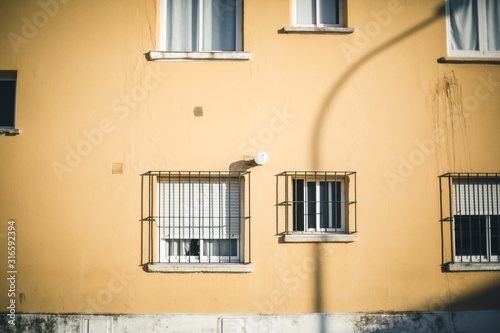Fachada amarilla con ventanas con rejas y sombras de farola