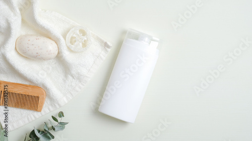 Hair care product design concept. SPA cosmetic bottle packaging, wooden hair comb, white towel, organic soap, luffa sponge on green background. Minimalist cosmetic product mockup, natural branding