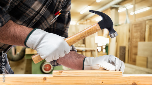 Close-up. Carpenter with his hands protected by gloves with a hammer and nails fixes a wooden board. Construction industry, carpentry workshop.