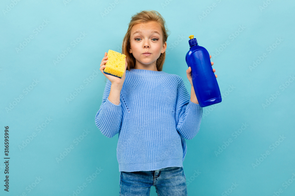 Girl is going to wash the dishes with washcloth and detergent isolated on blue background Girl is going to wash the dishes with washcloth and detergent isolated on blue background