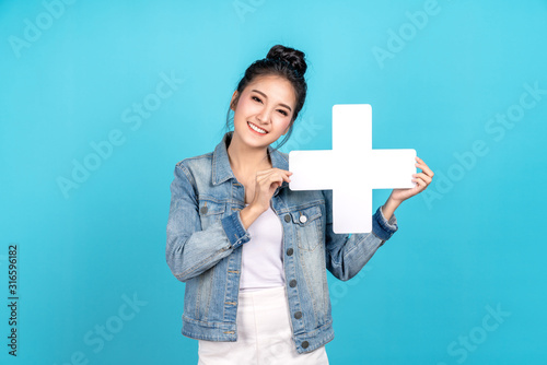 Happy asian woman smiling and holding plus or add sign on blue background. Cute asia girl smiling wearing casual jeans shirt and showing join sign for increse, upgrade and more benefit concept