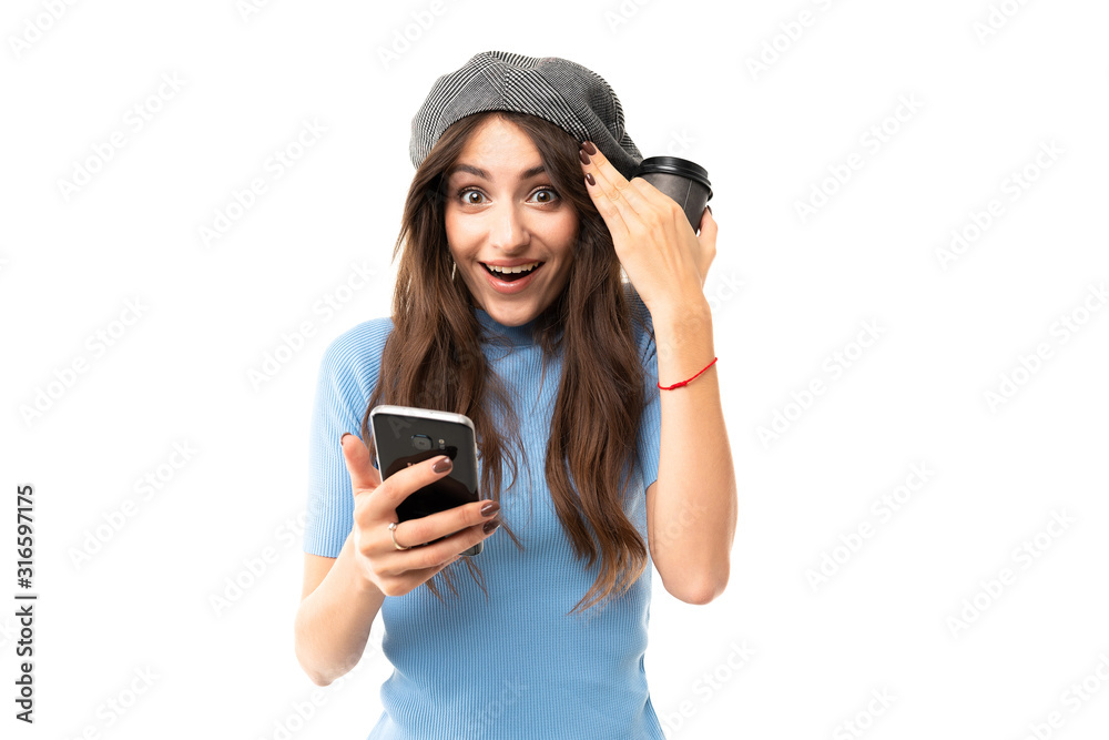 European joyful girl in a beret holds a cup of coffee and reads messages on the phone on a white background European joyful girl in a beret holds a cup of coffee and reads messages on the phone on a white background