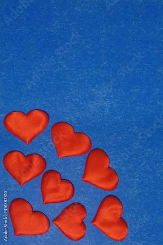 Vertical top view of red hearts in corner on blue cardboard background. Valentines Day concept, copy space.