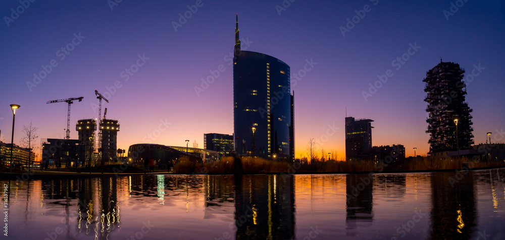 Milan cityscape at sunset with new skyscrapers in Porta Nuova financial and business district, reflected in a pond.