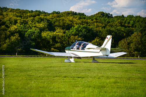 White light aircraft with one propeller and four seats at air show in western Germany. A plane standing on the lawn.