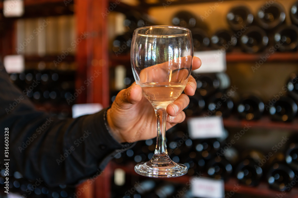 Εκτύπωση καμβά A glass of white wine on a man hand selective focus close up view against wine b
